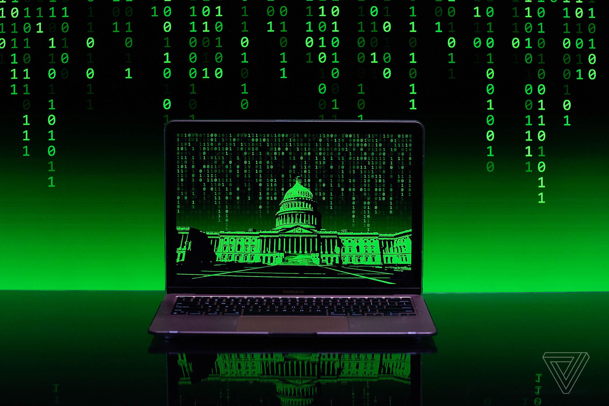 A matrix of green binary code flows down in the background of a laptop computer with a green hued image of the US capitol building