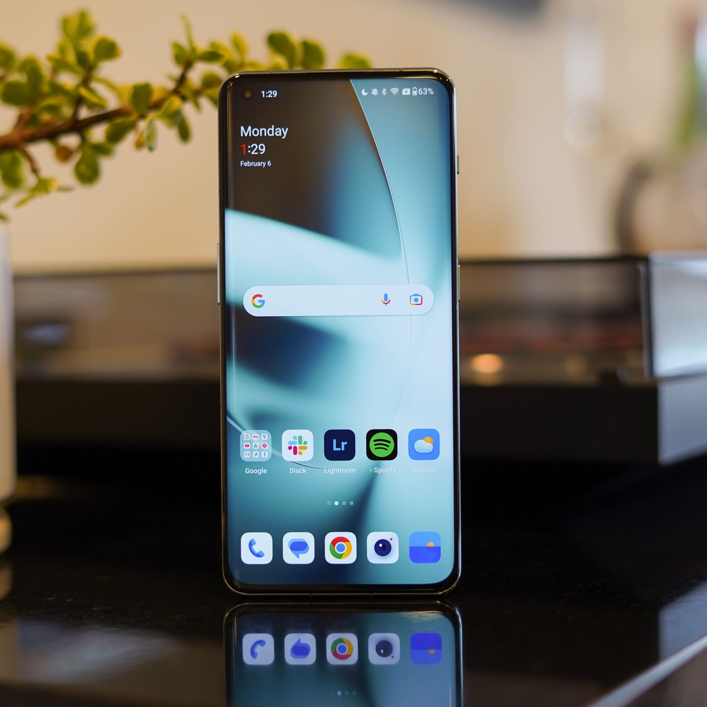 OnePlus 11 standing upright on a reflective countertop with homescreen on.