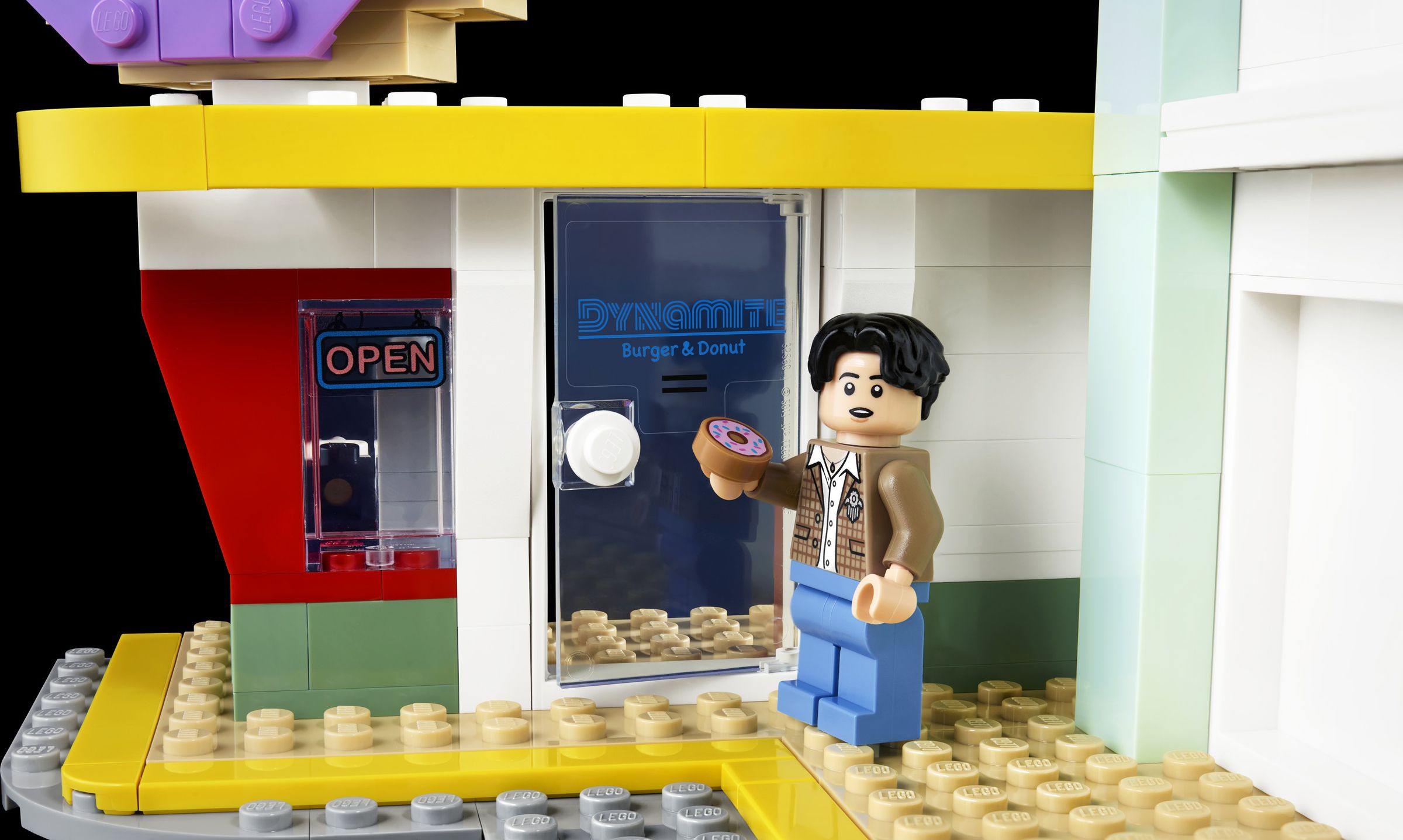 Lego figurine of Jungkook holding Lego donut outside a Lego donut shop.