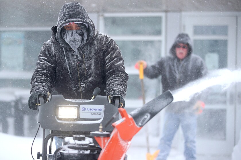 Man is covered in snow as he snow blows.