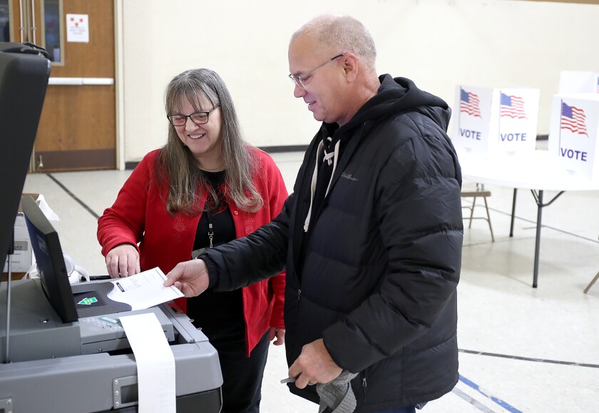 Man feeds ballot into voting machine as official watches.