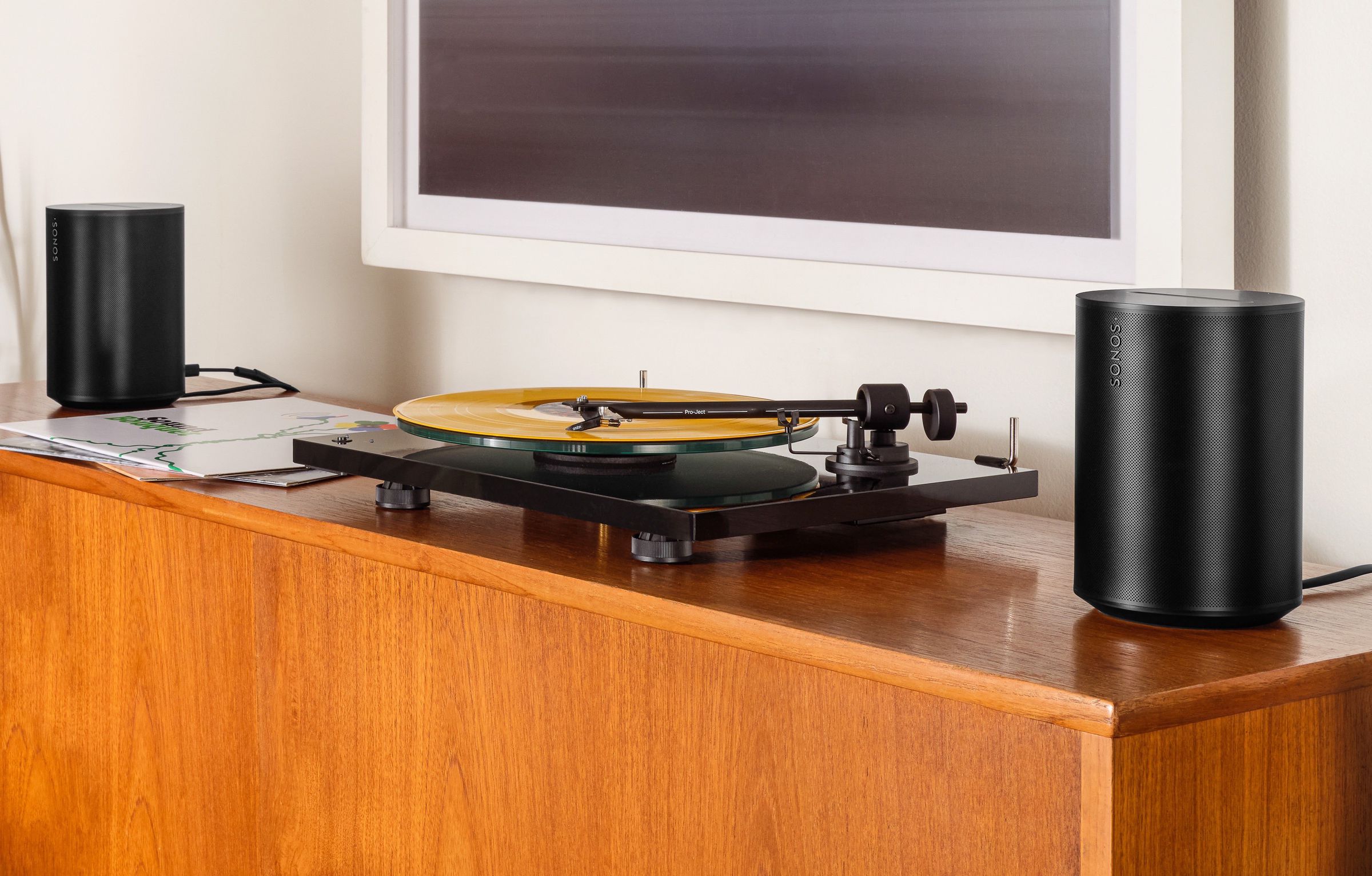 A marketing images of two Sonos Era 100 speakers with a turntable in the center.