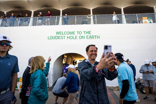 A fan takes a selfie in front of the tunnel to the 16th tee at the Phoenix Open. Above the entrance is a sign that says, “Welcome to the Loudest Hole on Earth.”