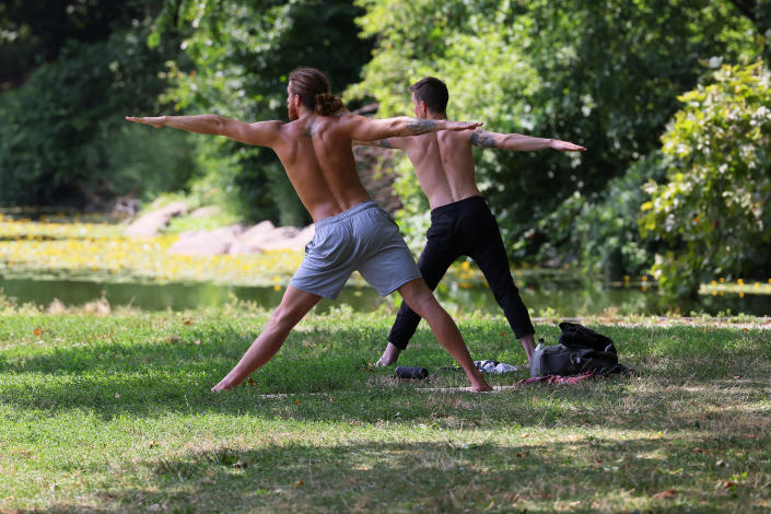 Two young men, arms and legs outstretched, on grass in a leafy setting.