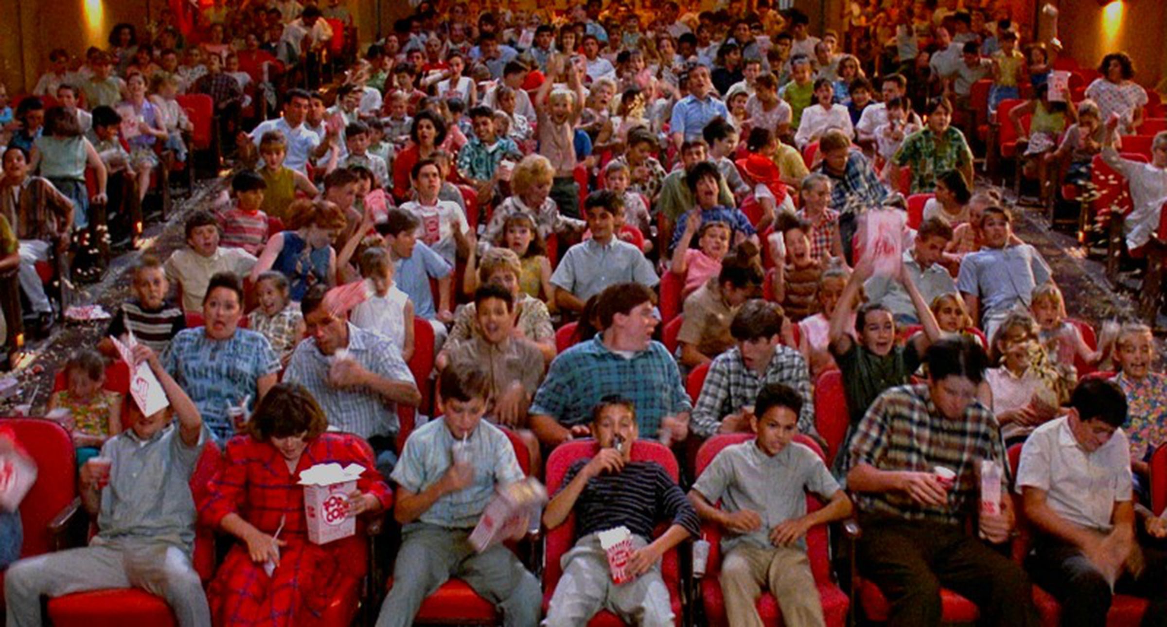 A bunch of unruly kids misbehaving in the seats of a movie theater.