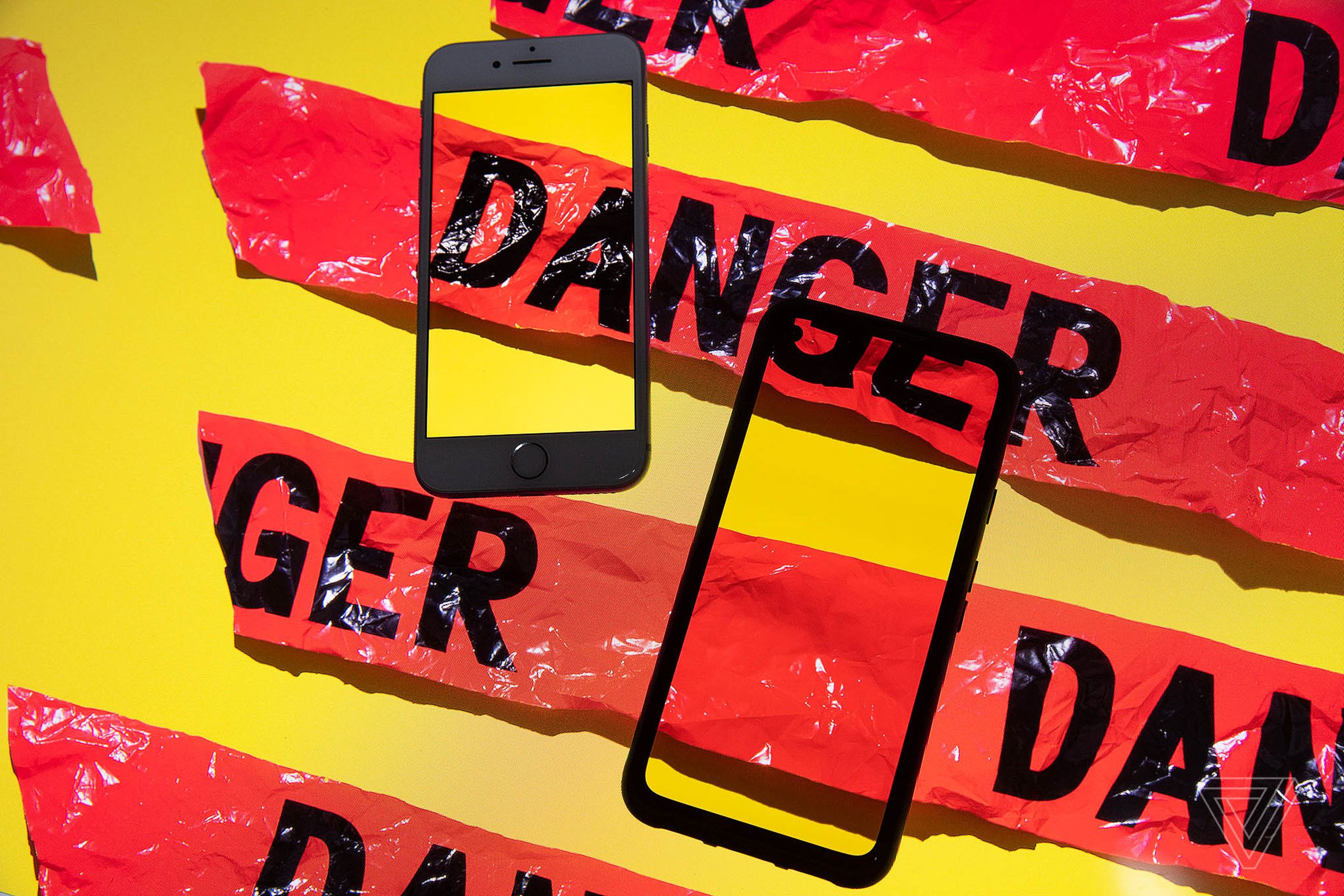 Illustration of two smartphones sitting on a yellow background with red tape across them that reads “DANGER”