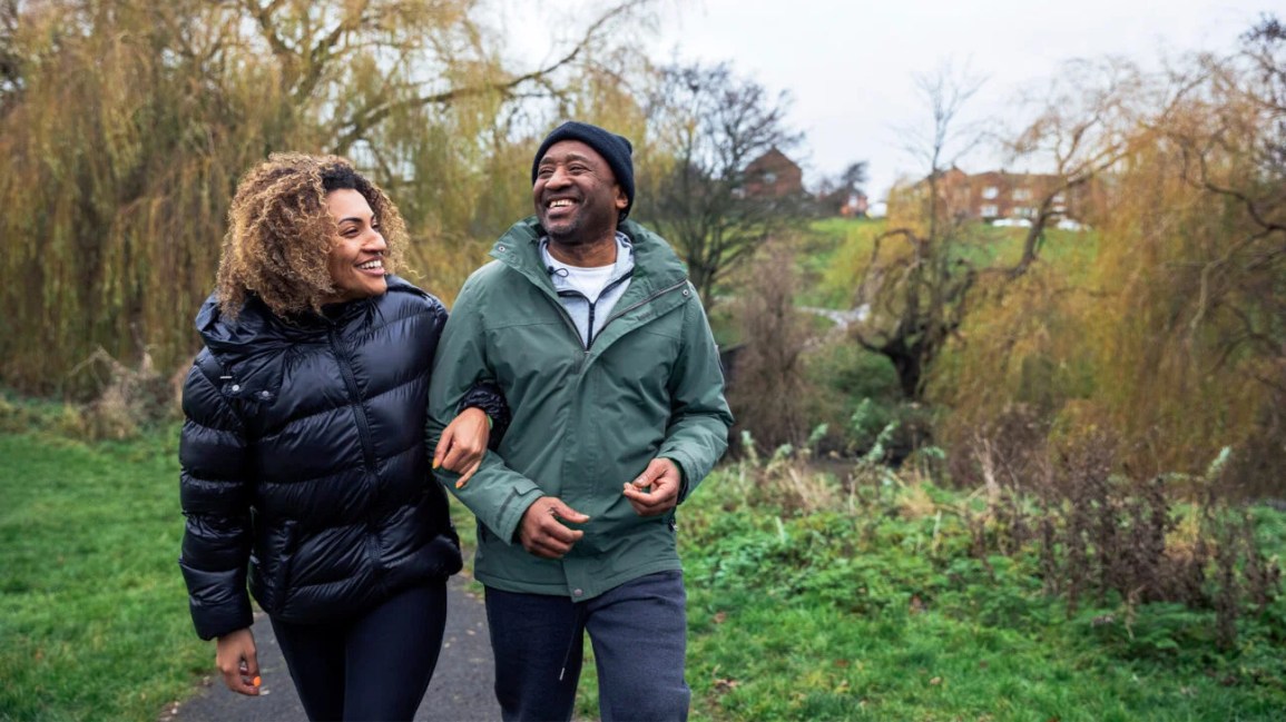 A father and adult daughter walk on a bike trail along a river