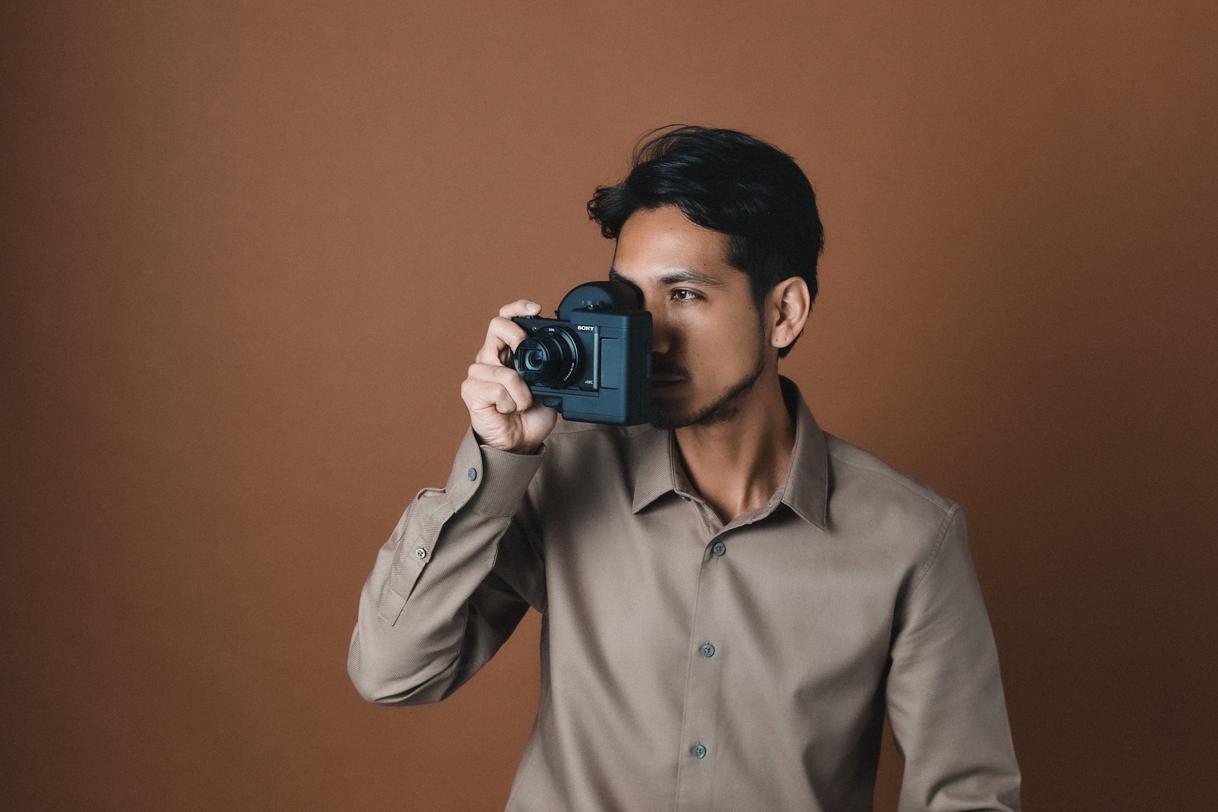 A person holding the Sony DSC-HX99 compact camera to their eye with a QD Laser Retissa Neoviewer retinal projection viewfinder.