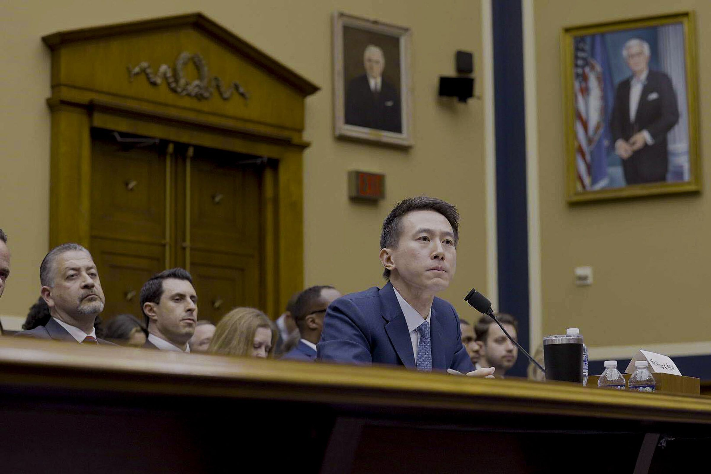 Shou Zi Chew is seated for a hearing. Portraits of American political figures hang on the wall behind him.