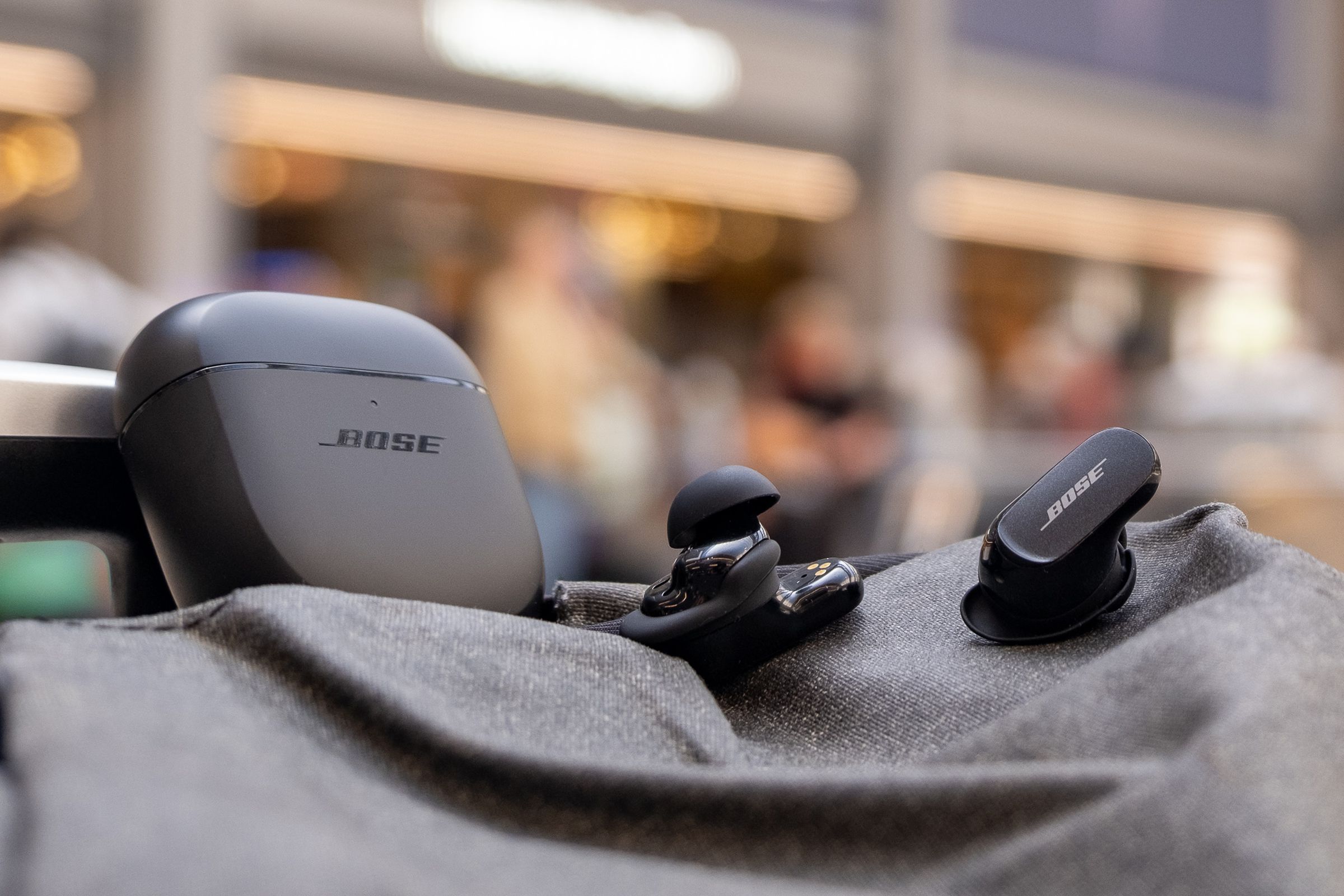 An image of the Bose QC Earbuds II on top of a backpack in a train terminal.