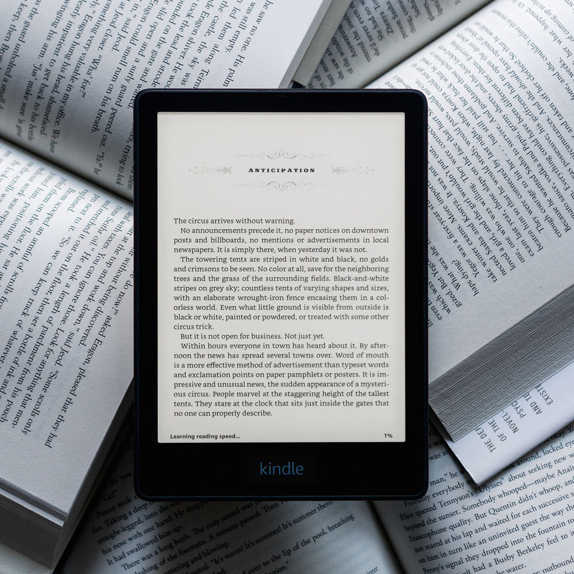 The Kindle Paperwhite e-reader turned on resting on a bunch of analog books.