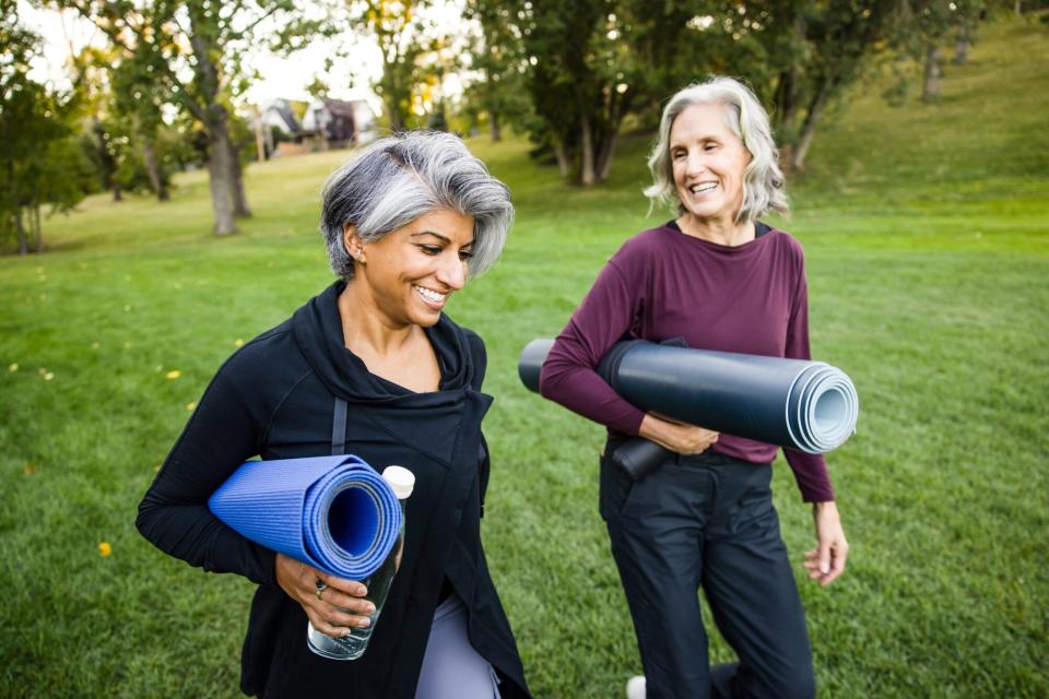 Happy mature women friends with yoga mats walking in park