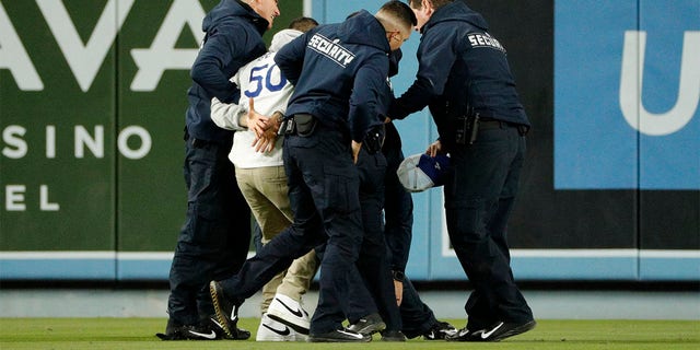 Security personnel remove a Dodger fan who ran onto the outfield during the game against the Arizona Diamondbacks at Dodger Stadium on March 30, 2023, in Los Angeles, California. 