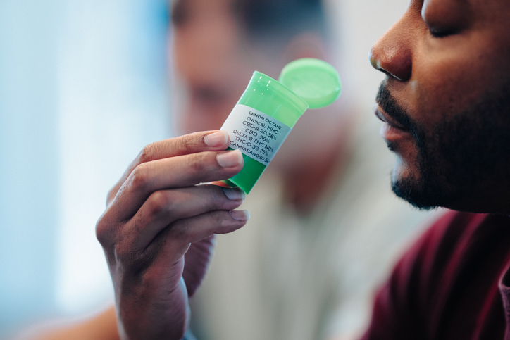 Man smelling cannabis buds in bottle