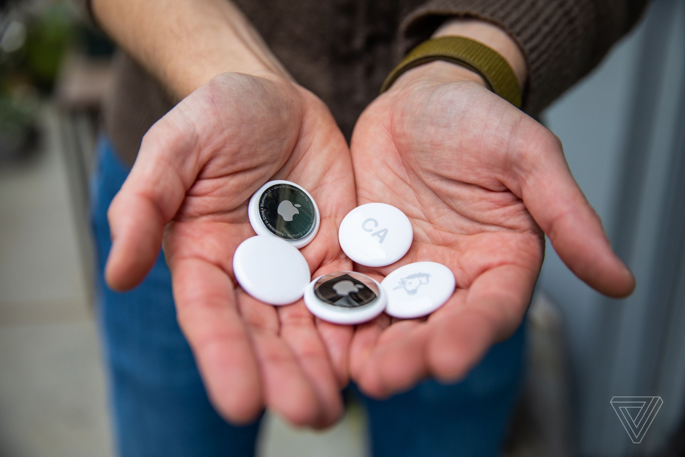 A close-up image depicting a set of hands holding a selection of Apple AirTags.