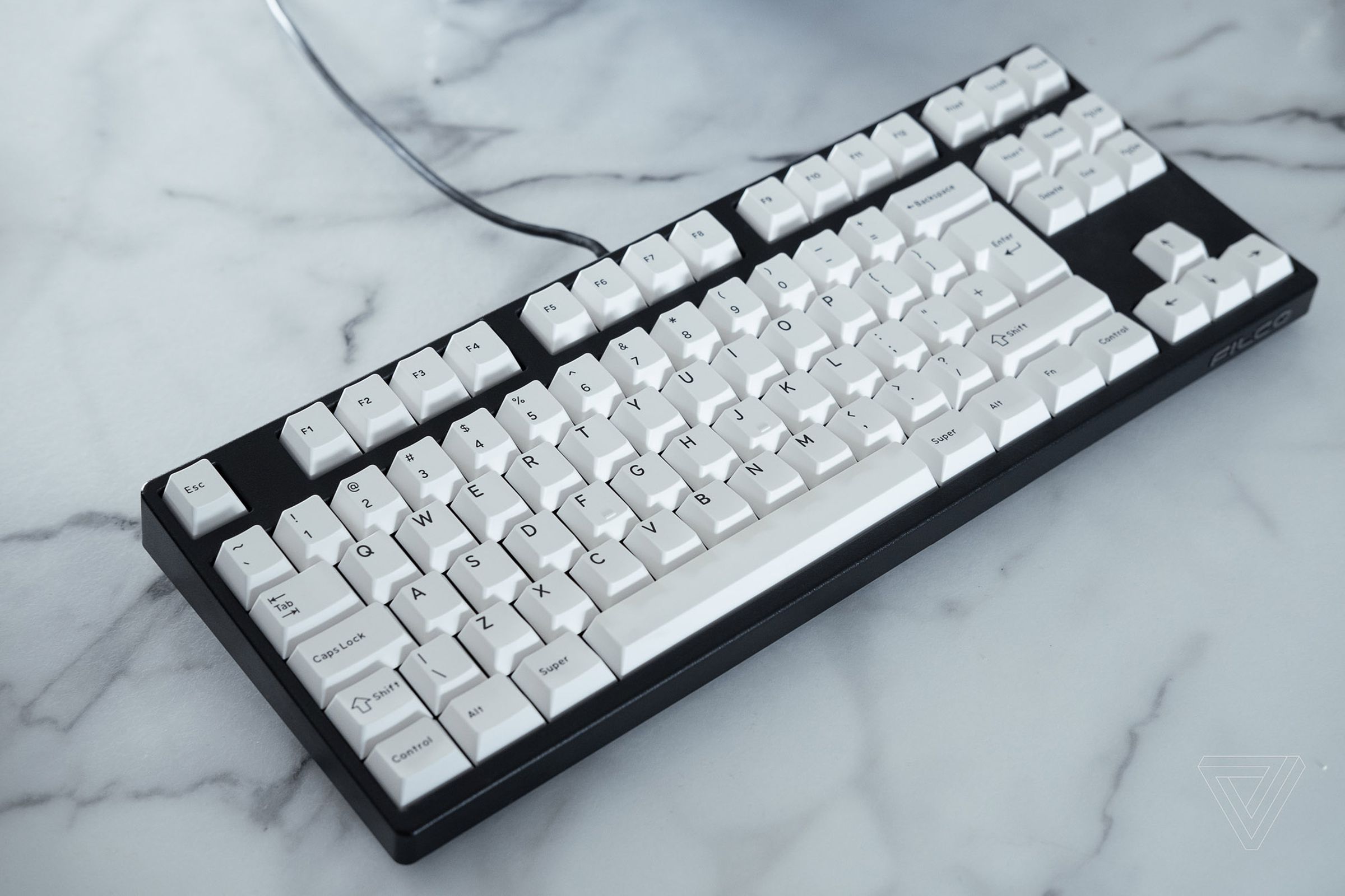 A black mechanical keyboard with white keycaps on a white marble table.