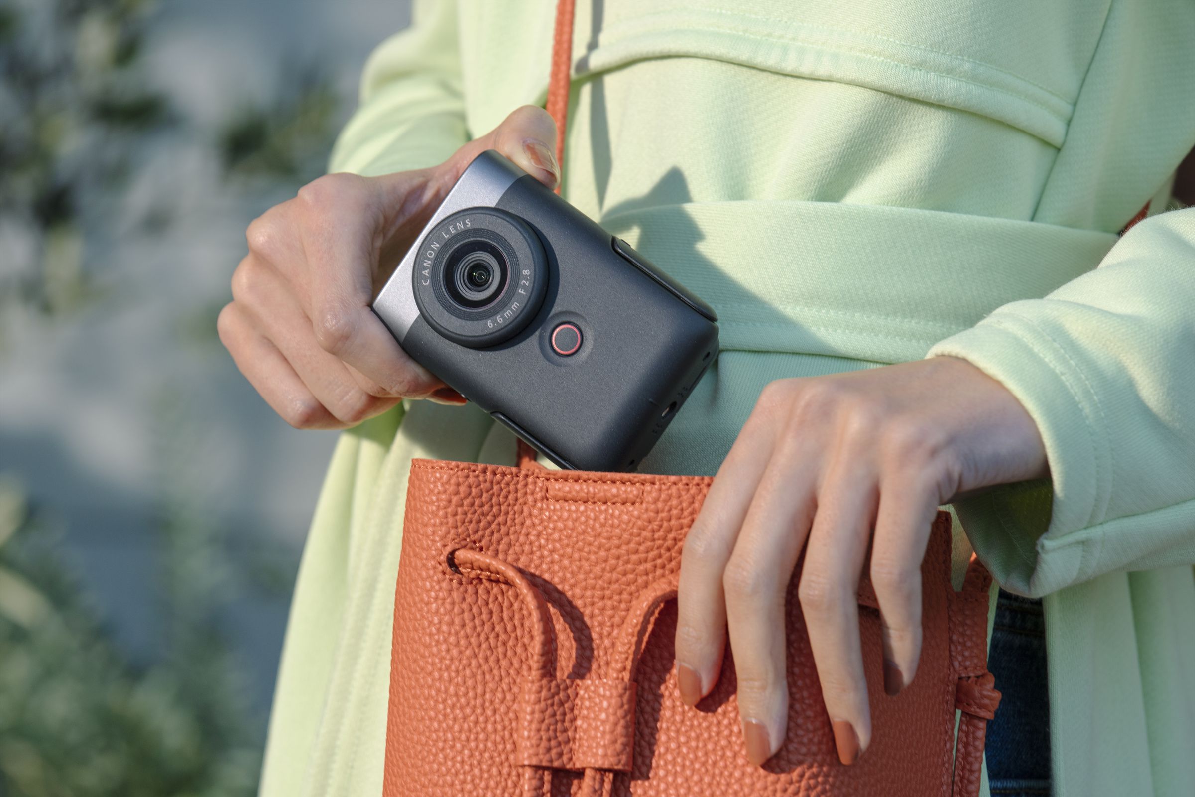 A person removing the Canon PowerShot V10 vlogging camera from an orange handbag.