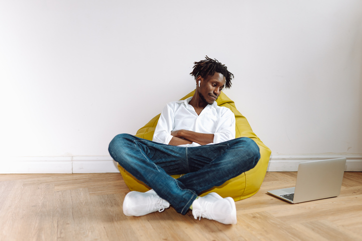 Podcasts and music for life. Smiling multiracial male with earphones sit in beanbag chair in studio