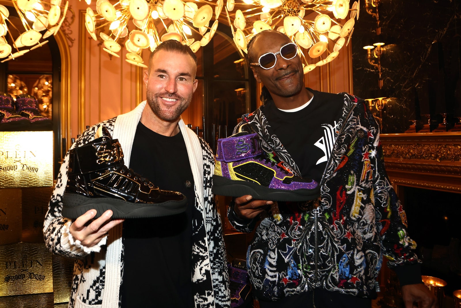 Philipp Plein poses next to Snoop Dogg each holding a sneaker.