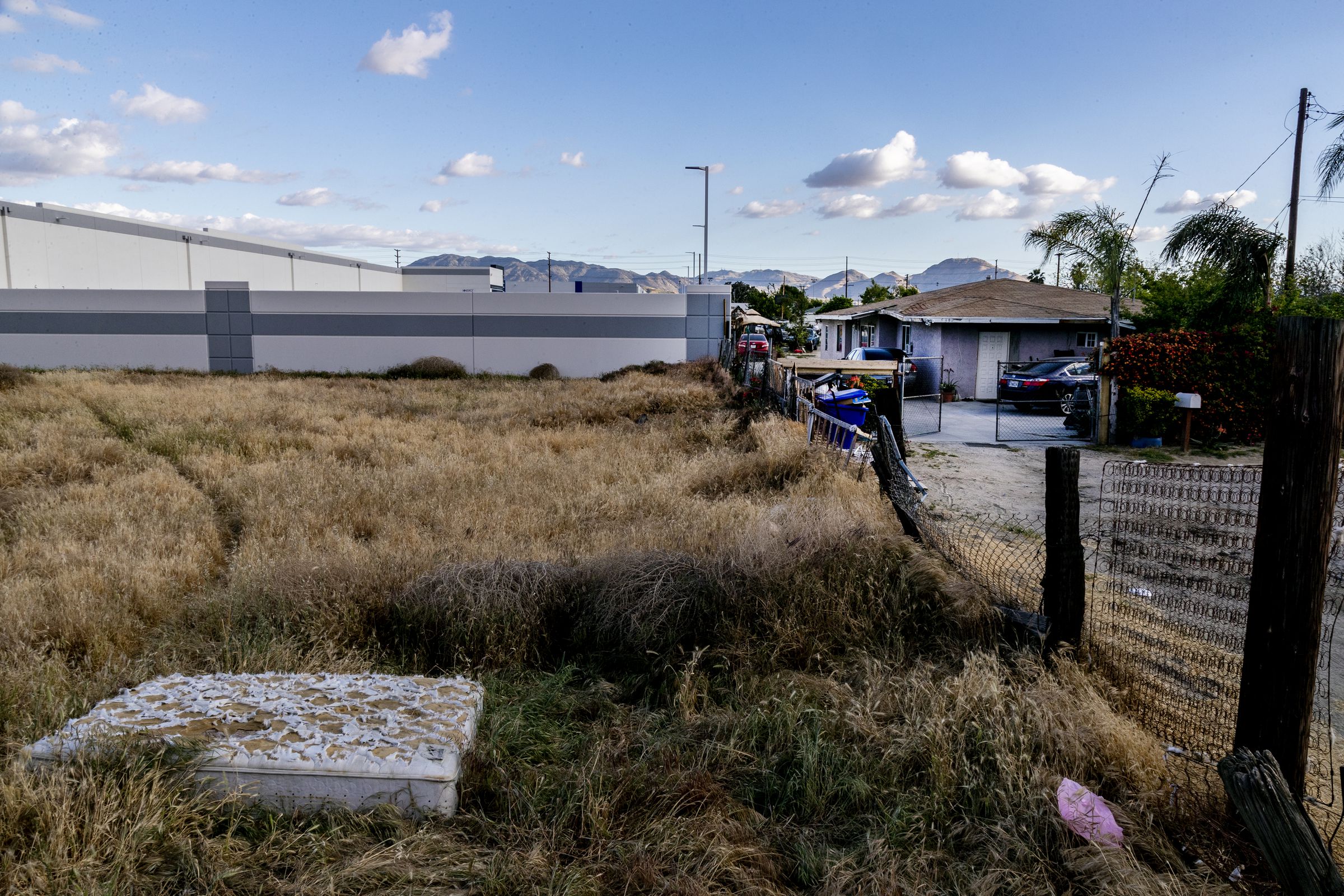 A large warehouse shares a fence line with a small house.