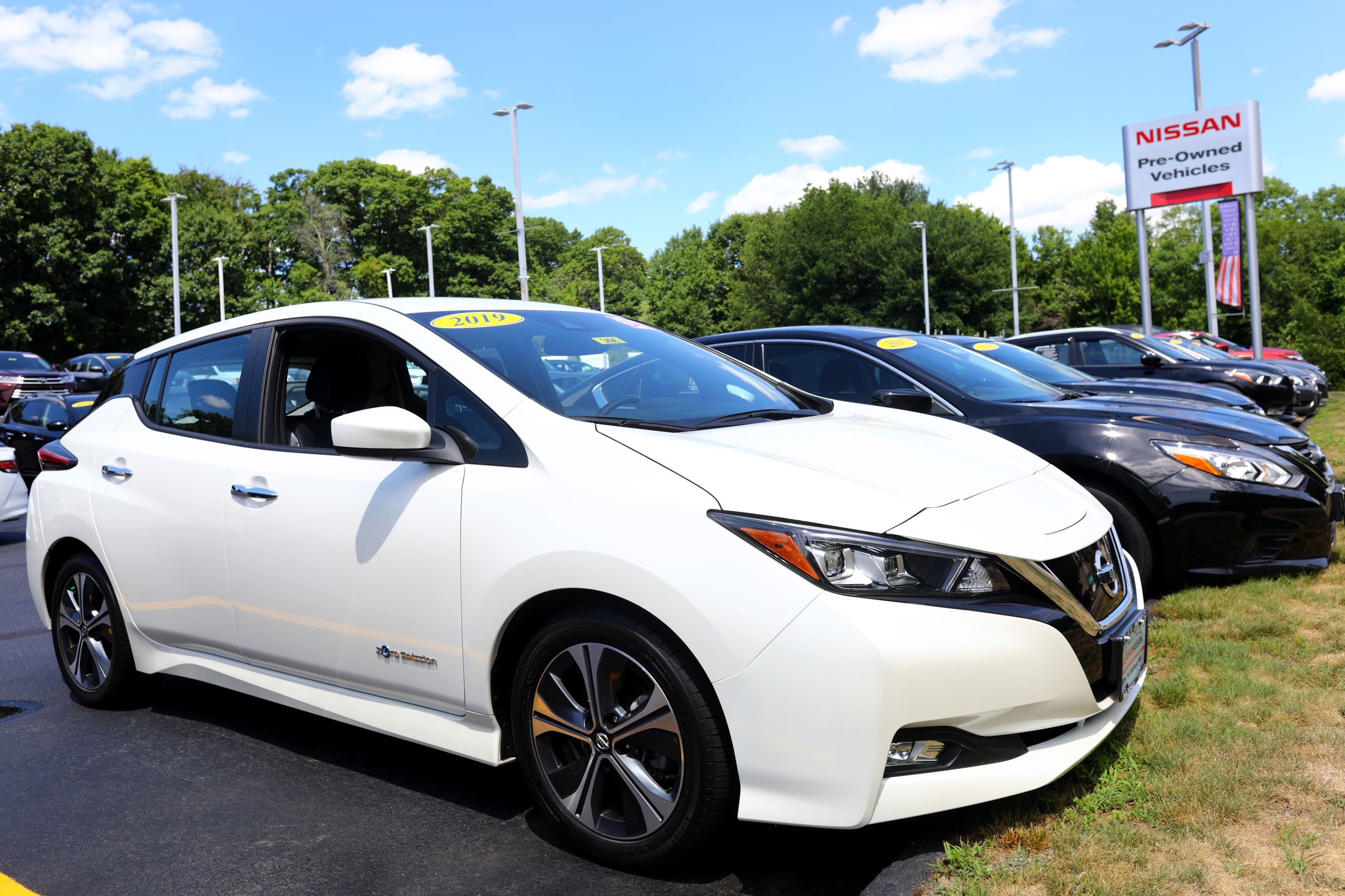 A white electric vehicle in a parking lot with rows of other cars behind it.