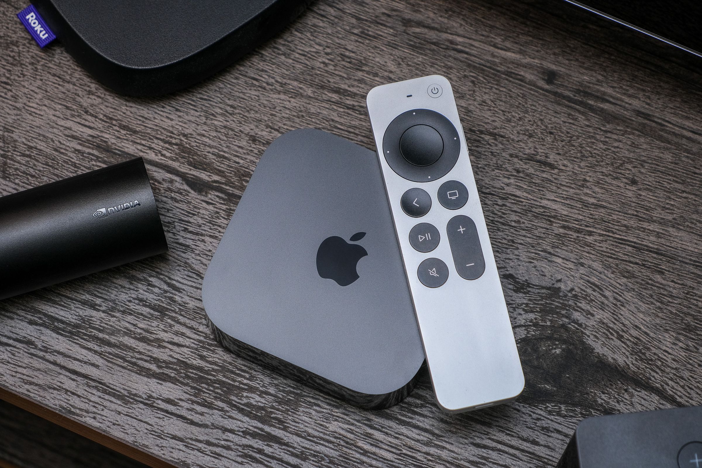 A photo of the third-gen Apple TV 4K on a TV stand surrounded by competing products from Amazon, Roku, and Nvidia.