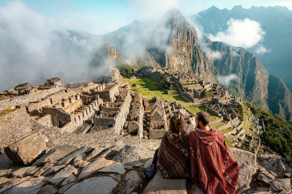 Couple dressed in ponchos watching the ruins of Machu Picchu