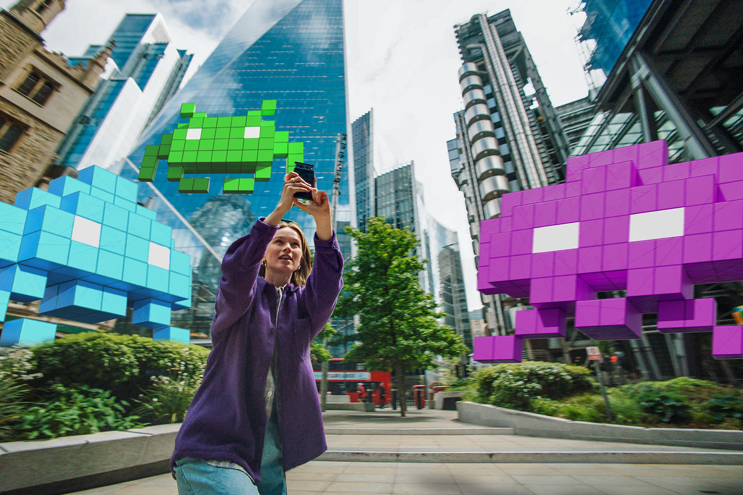 In a promotional photo for Space Invaders: World Defense, three large Space Invaders aliens next to a person holding a Pixel smartphone.