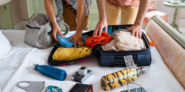 Two people pack luggage on a bed.