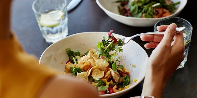 Woman eats healthy meal across from somone.