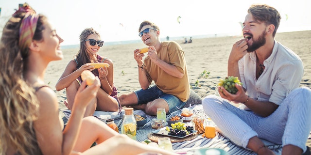 People eat while on a beach picnic.