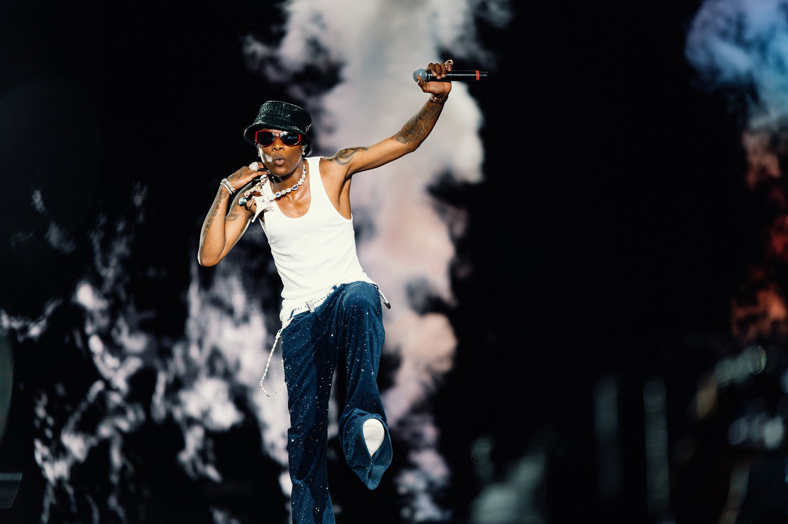 Musical artist Wizkid performing wearing a white tank top jeans sunglasses and a black bucket hat