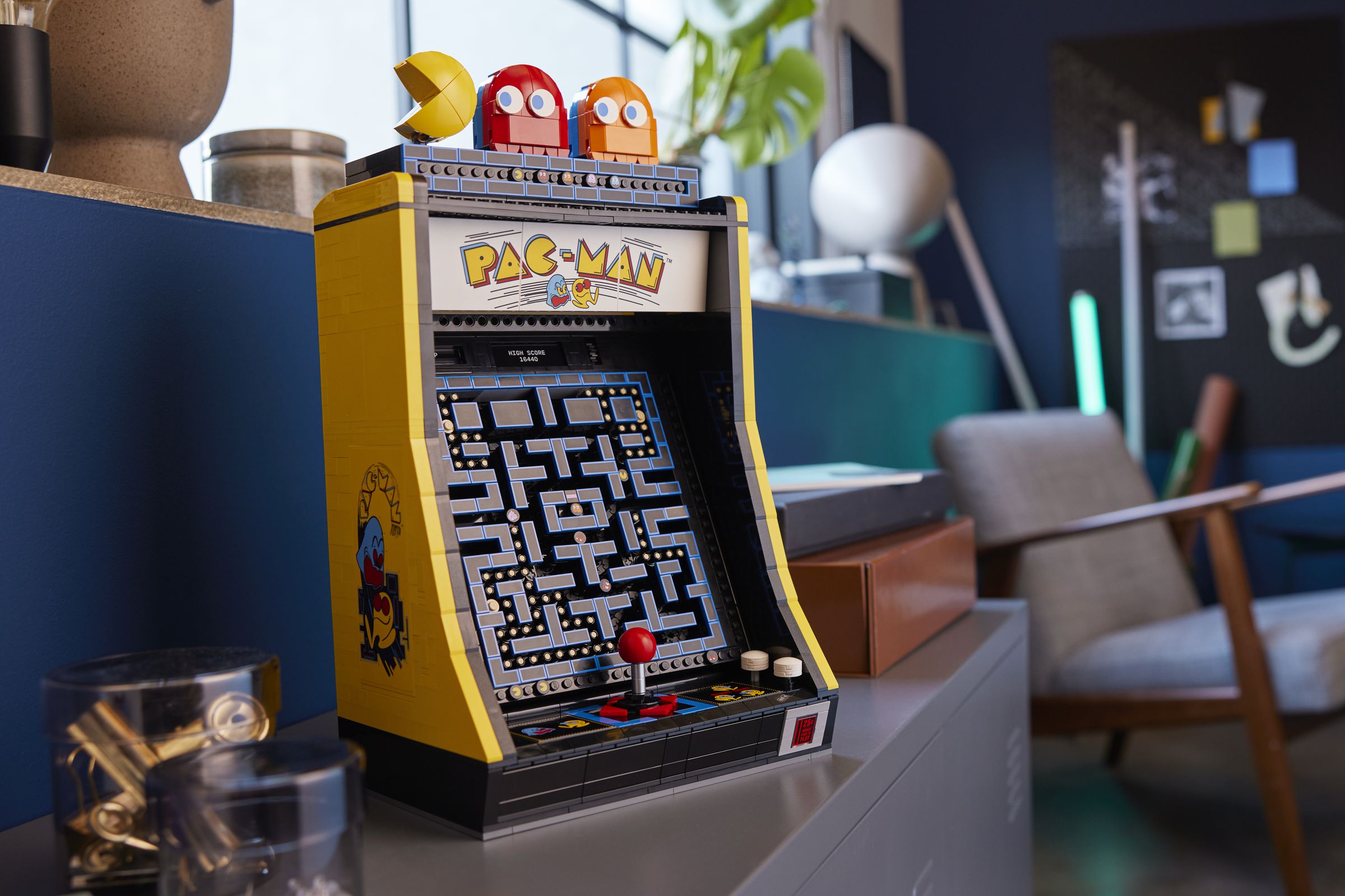 A lego pac-man arcade cabinet in a busy room.