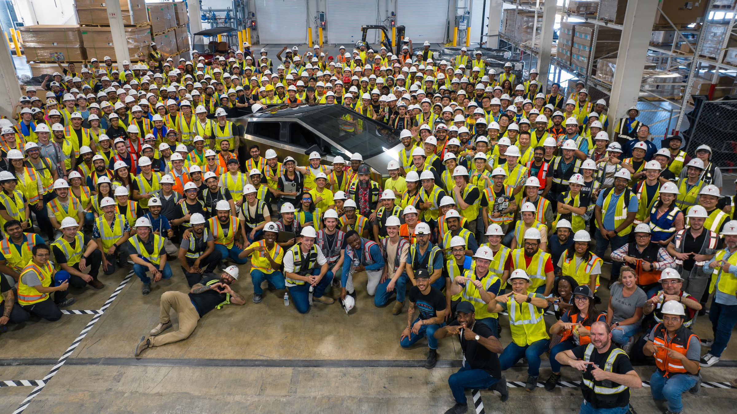 Tesla Cybertruck pickup shown surrounded by factory workers.