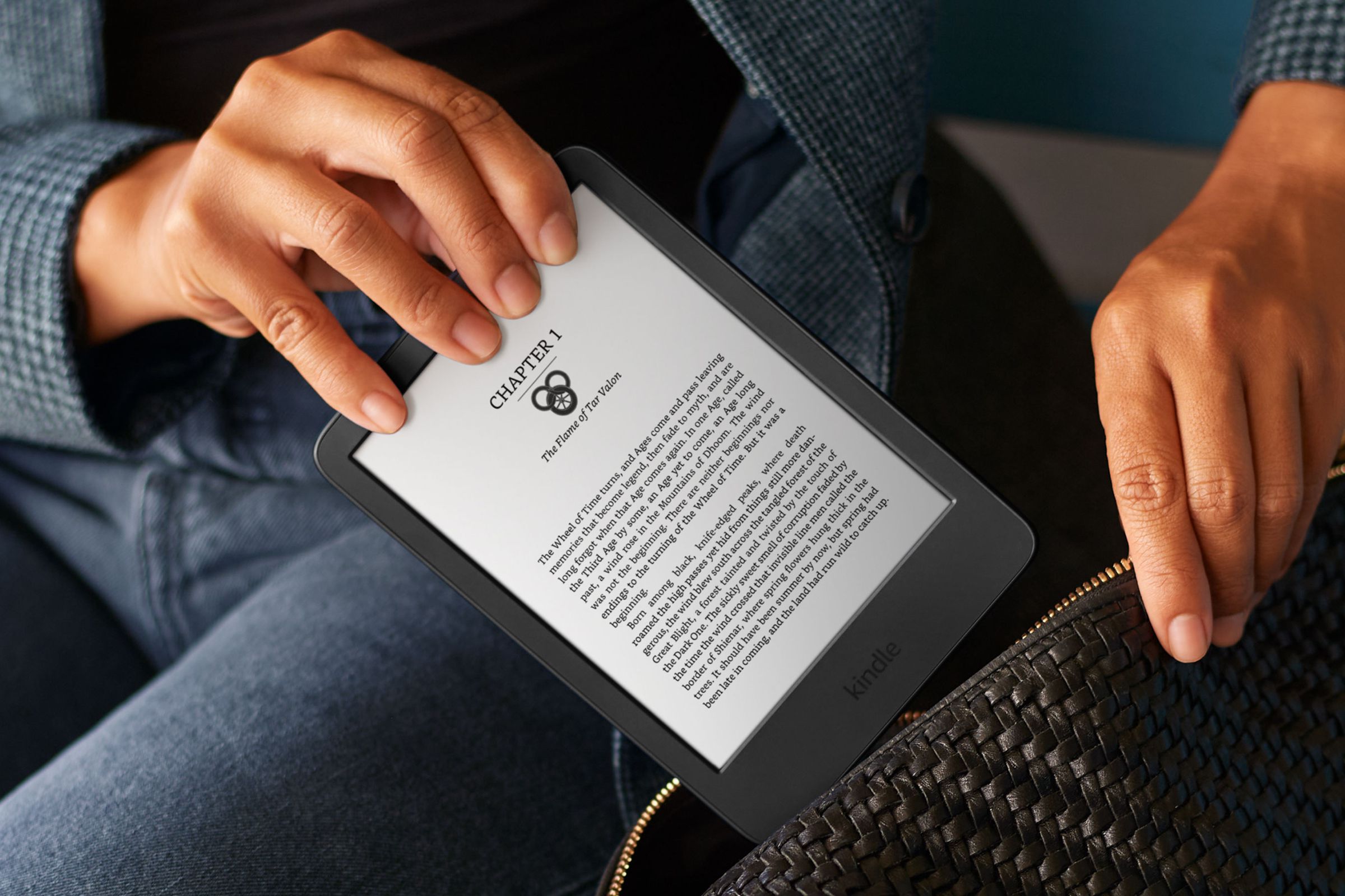 A close-up image of a pair of hands placing Amazon’s 11th-gen Kindle in a purse.