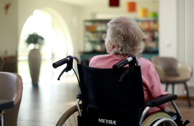 An elderly woman sits in the recreation room of a retirement home as visits have been restricted due to the coronavirus disease (COVID-19) concerns in Grevenbroich (credit: REUTERS)