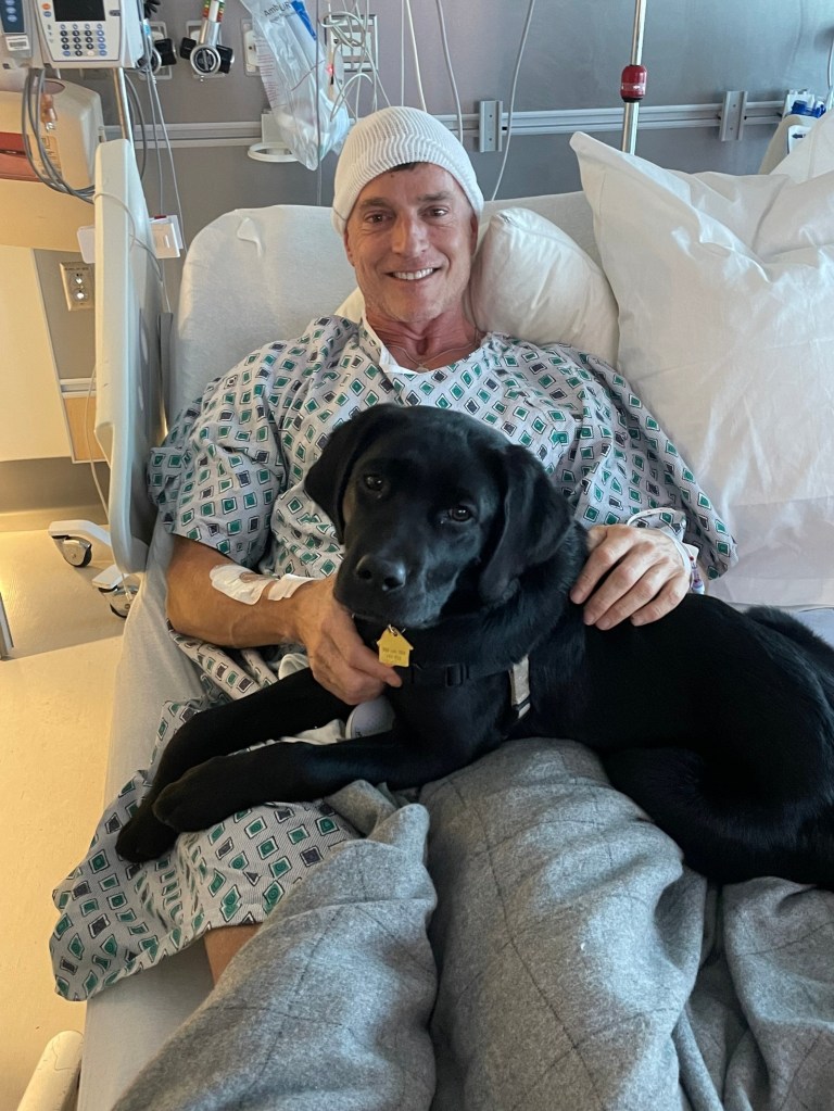 Photo of man in a hospital bed with a dog. 