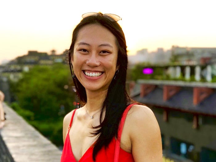 Angelina Lu smiling while standing on a balcony and wearing a red dress.