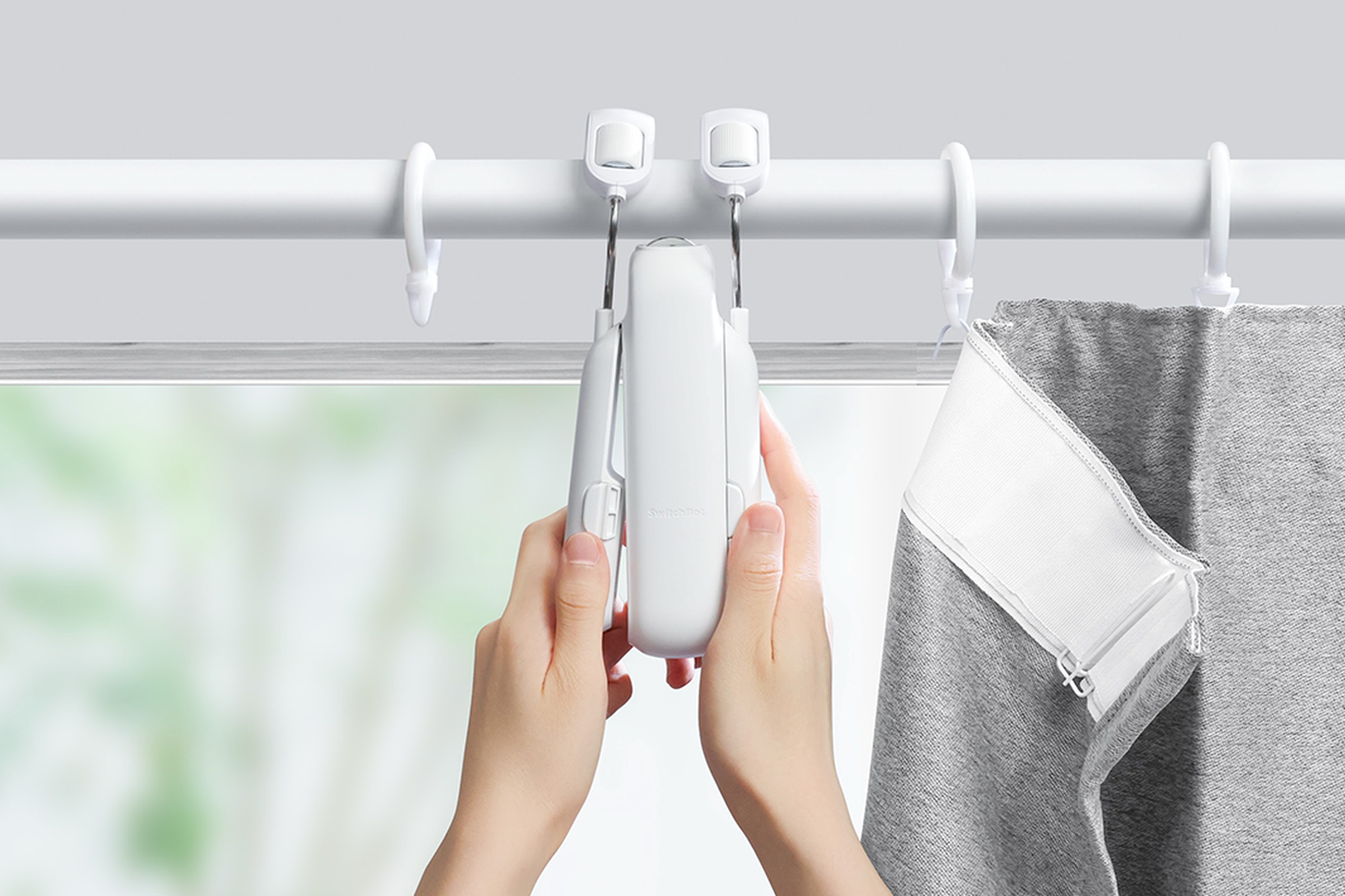 A picture of a person’s hands installing the SwitchBot 3 on a telescoping curtain rod.