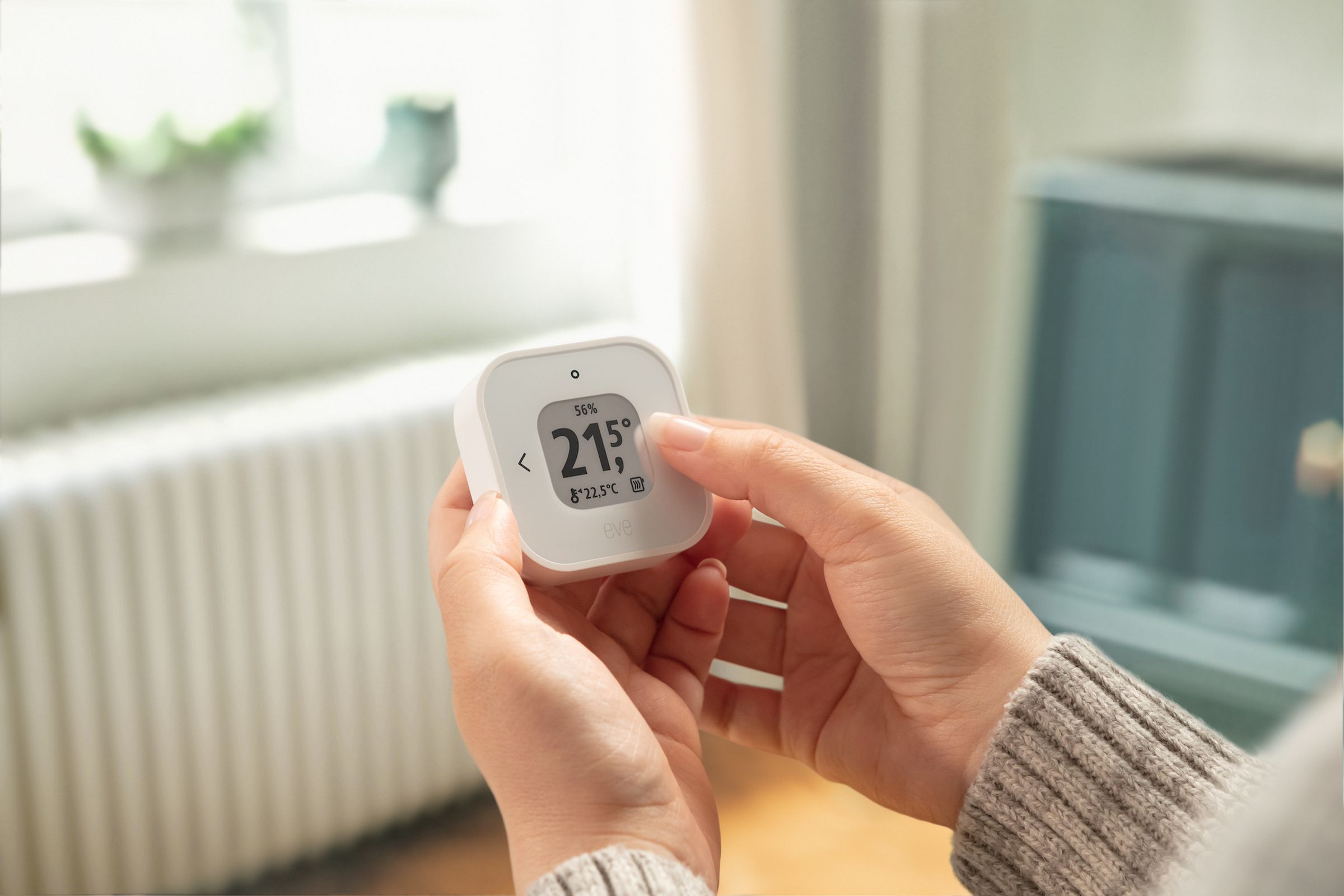 A pair of hands holding the Thermo Control sensor, which is small, white, squareish, with rounded corners on the body and on the small screen, which shows the temperature.