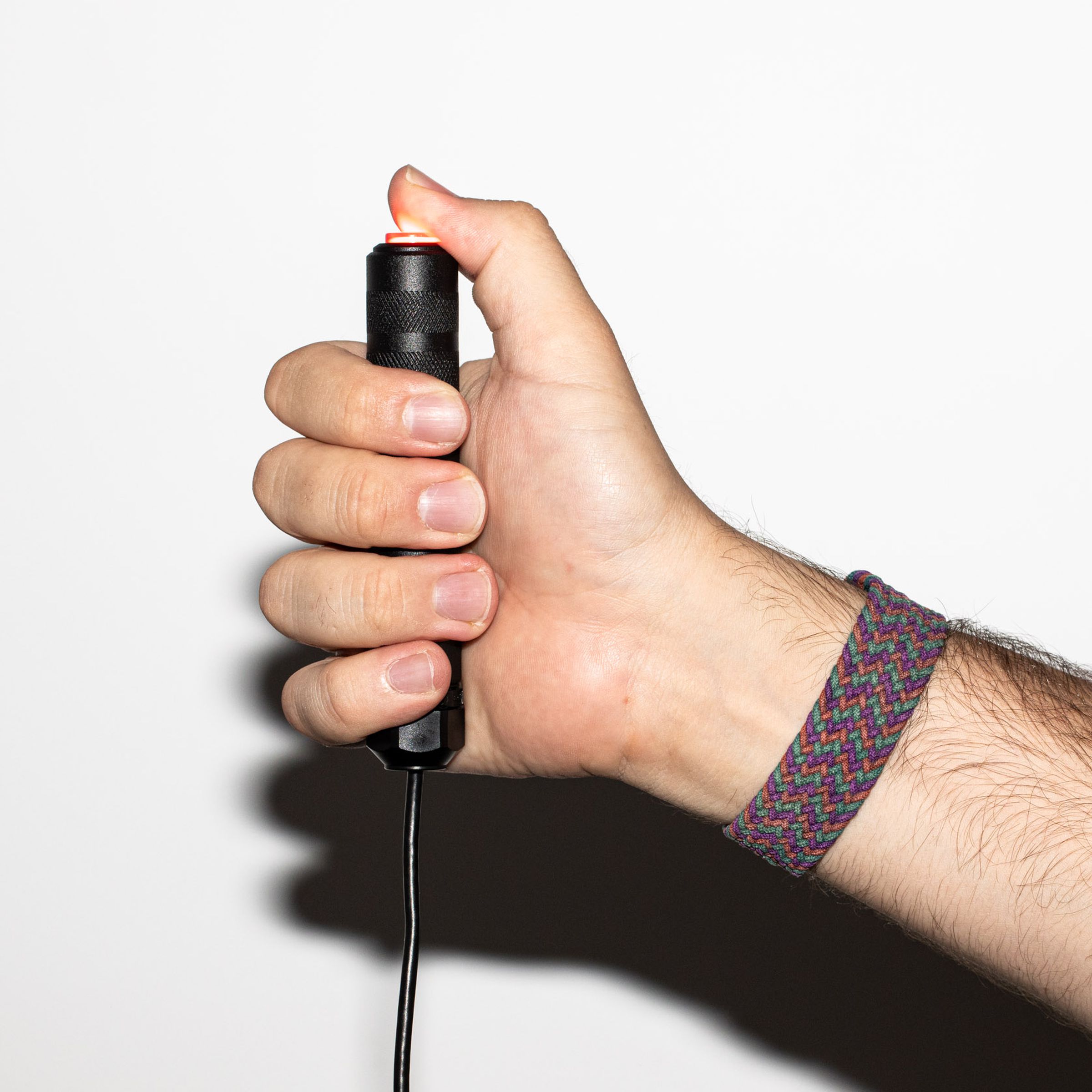 An arm grasps a fist-sized round black metal rod with a glowing red button on top, just underneath the thumb.