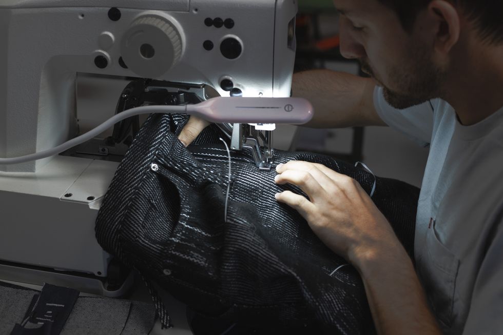 a man sits at a sewing machine finishing pants from the eckhaus latta spring 2024 runway unspun collaboration