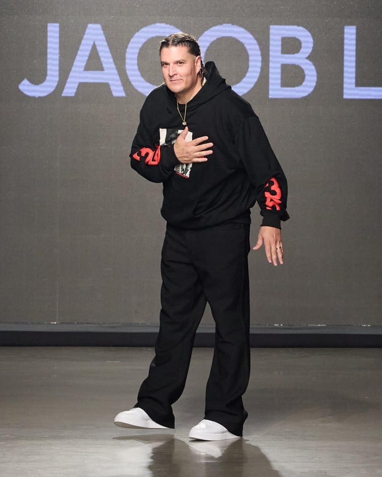 Designer Justin Jacob Louis on the runway for his show, wearing white shoes, black pants and top.