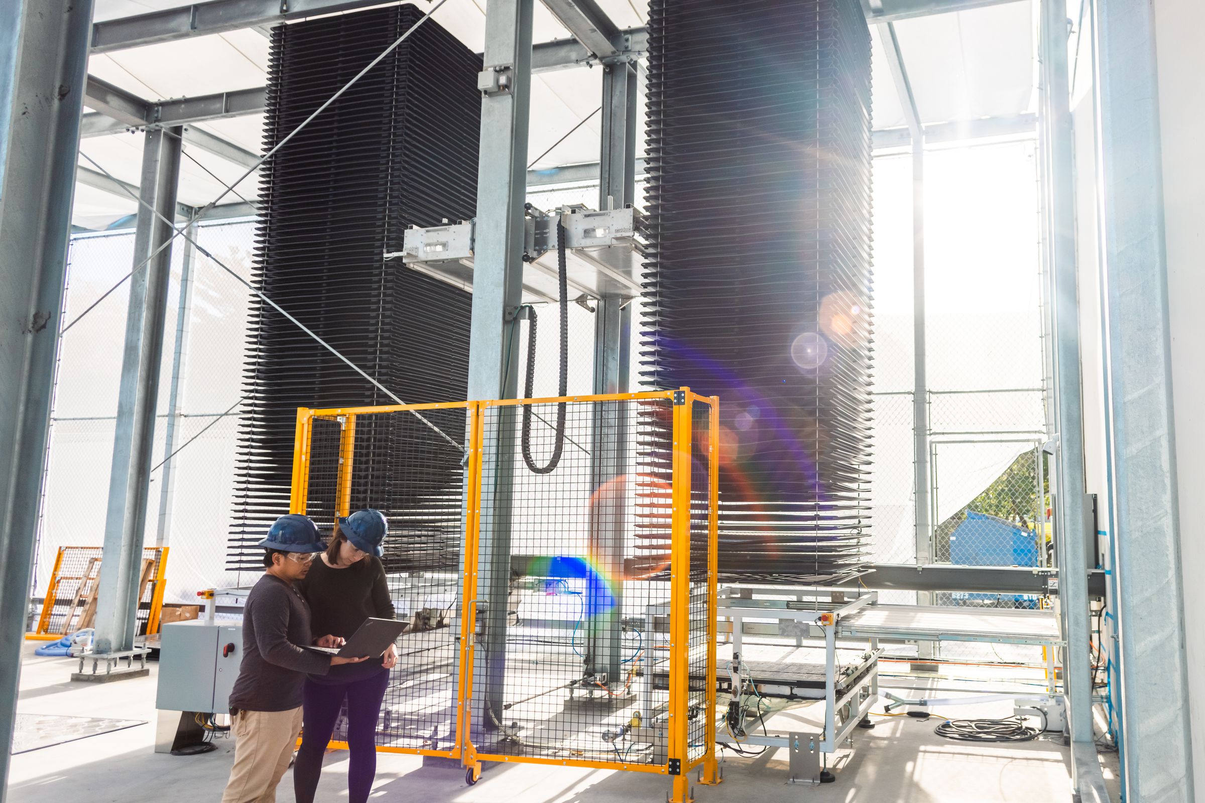 Two people wearing hard hats stand in front of two towering columns that filter CO2 out of the ambient air.