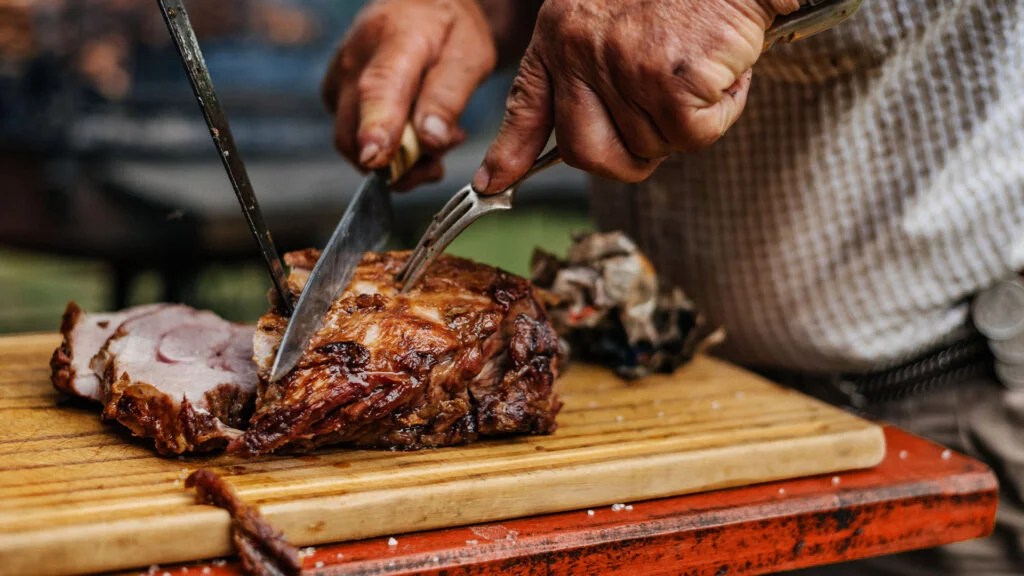 A man slices a piece of barbecued meat