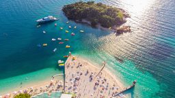 Aerial view of a beautiful white sand beach with turquoise water and relaxing people on a sunny day. Ksamil, Albania.