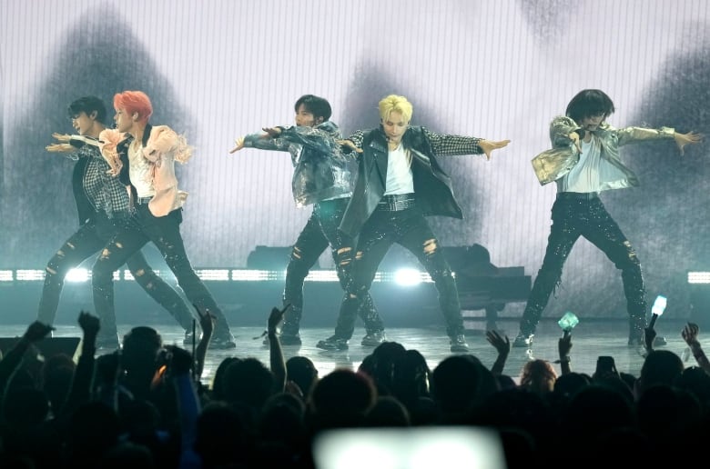 A five-person boy band performs on a stage in front of a crowd.