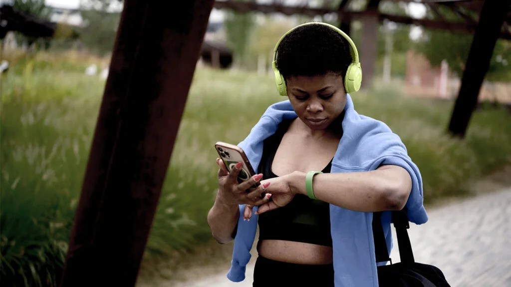 A woman checks her smartphone and smartwatch to record her daily physical activity outside in nature