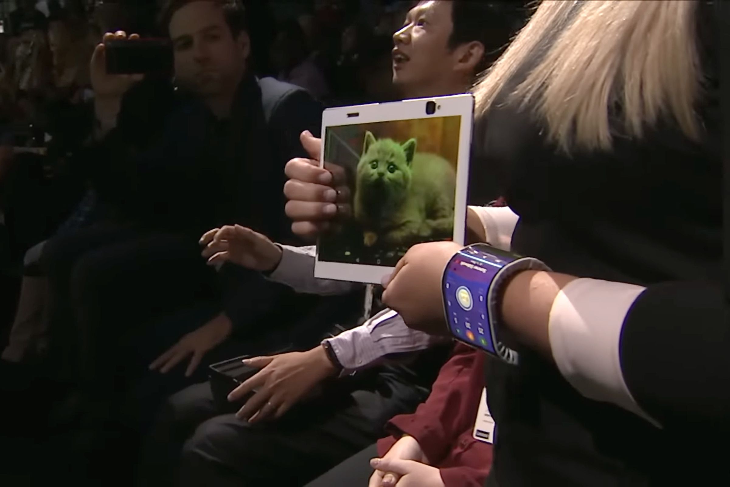 Screenshot of a woman holding a bendable tablet prototype (displaying a photo of a cat) and wearing a bending phone prototype wrapped around her left wrist.