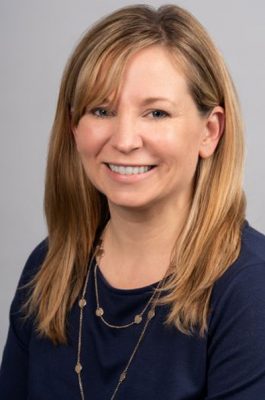 A woman smiles for a headshot against a grey backdrop.